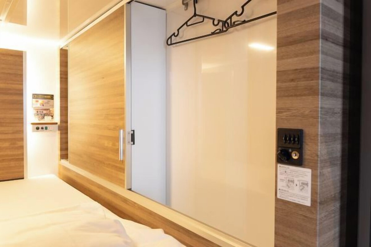 A hotel room with a wooden wardrobe, a bed, and a control panel on the wall.