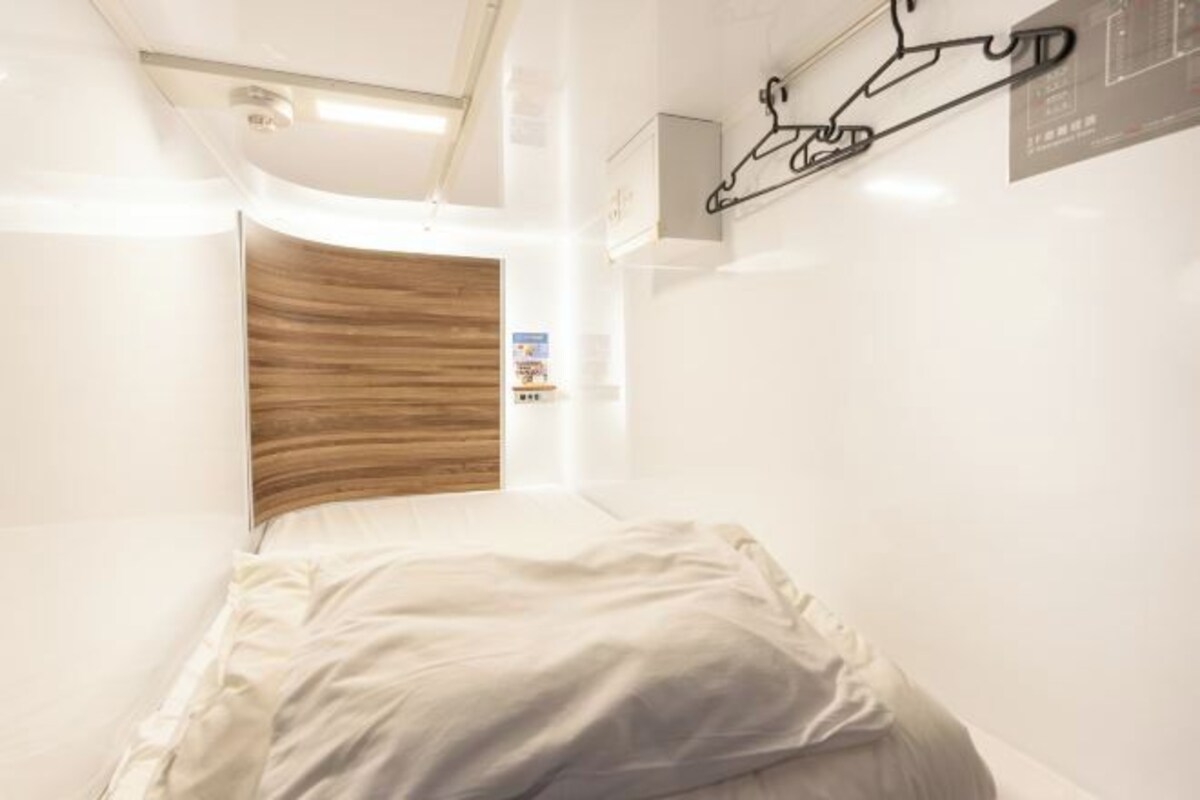 A narrow hotel room with a bed, a wooden panel wall, and a wall-mounted light fixture.