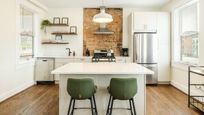 A modern kitchen with a central island, white cabinetry, a brick accent wall, and a stainless steel refrigerator. - Walk to Rhinegeist | Findlay Market| Streetcar (Cincinnati)