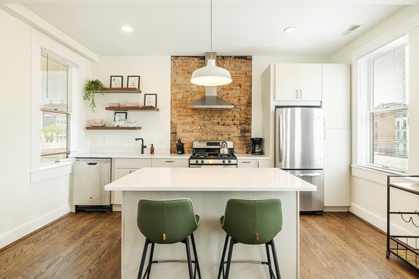 A modern kitchen with a central island, white cabinetry, a brick accent wall, and a stainless steel refrigerator.