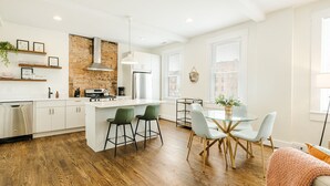 A modern kitchen with white cabinetry, a brick accent wall, and a central island with bar stools. - Walk to Rhinegeist | Findlay Market| Streetcar (Cincinnati)