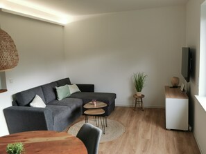 A modern living room with a grey sofa, a small round table, a TV on the wall, and a wooden cabinet. - Neue Ferienwohnung im Herzen Schweichs - mit Großem Garten und Ruhiger Terrasse (Schweich)