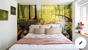 Une chambre avec une grande fresque représentant une forêt sur le mur, un lit avec une literie blanche et une petite table de chevet avec une lampe.