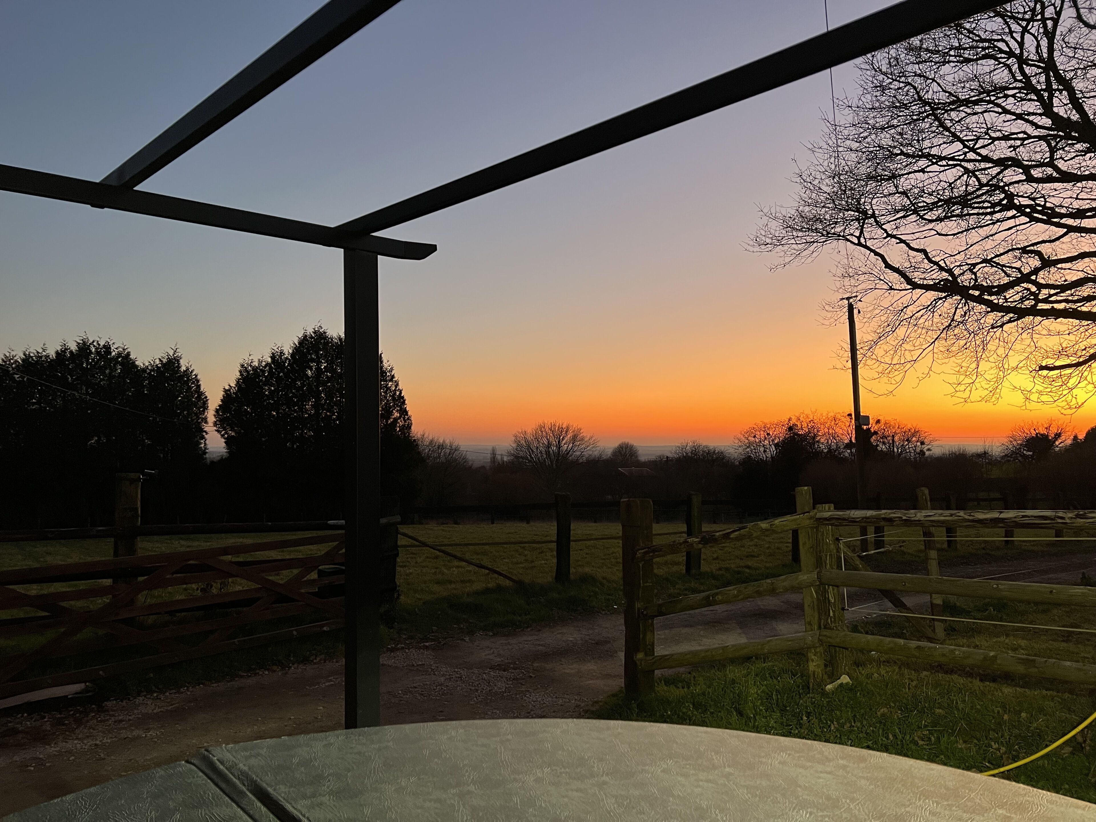 A sunset view from a covered outdoor area with a wooden fence and a metal structure.