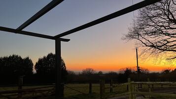 A sunset view from a covered outdoor area with a wooden fence and a metal structure.