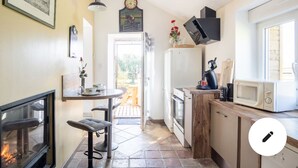 Une cuisine compacte avec une cheminée, un coin repas avec une table et des chaises, et une vue sur l’extérieur.