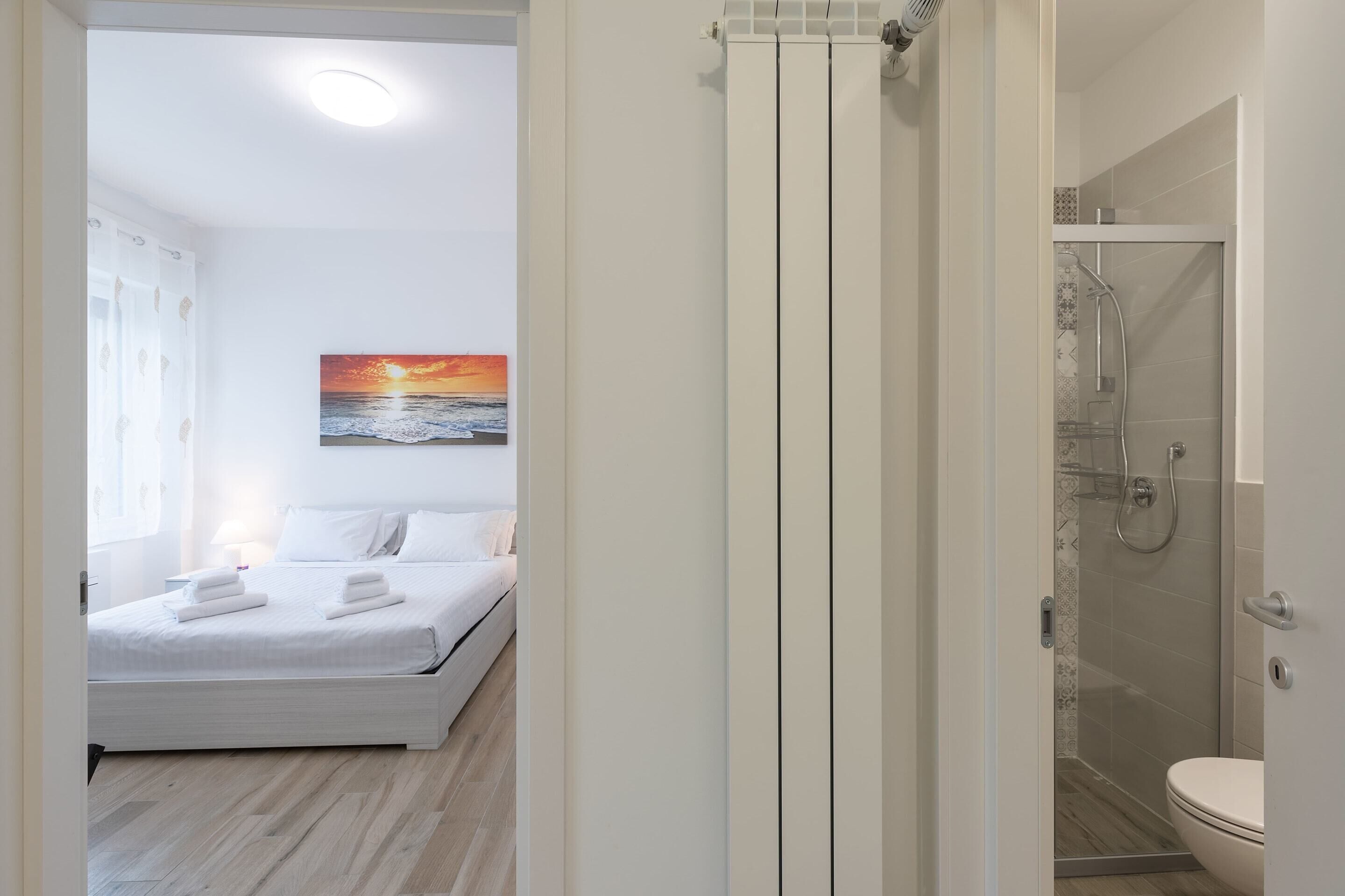 Een moderne hotelkamer met een bed, een douche en een schilderij van een zonsondergang.