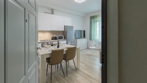 Una cocina moderna con armarios blancos, una mesa de comedor con sillas, horno empotrado y un televisor de pantalla plana montado en la pared.