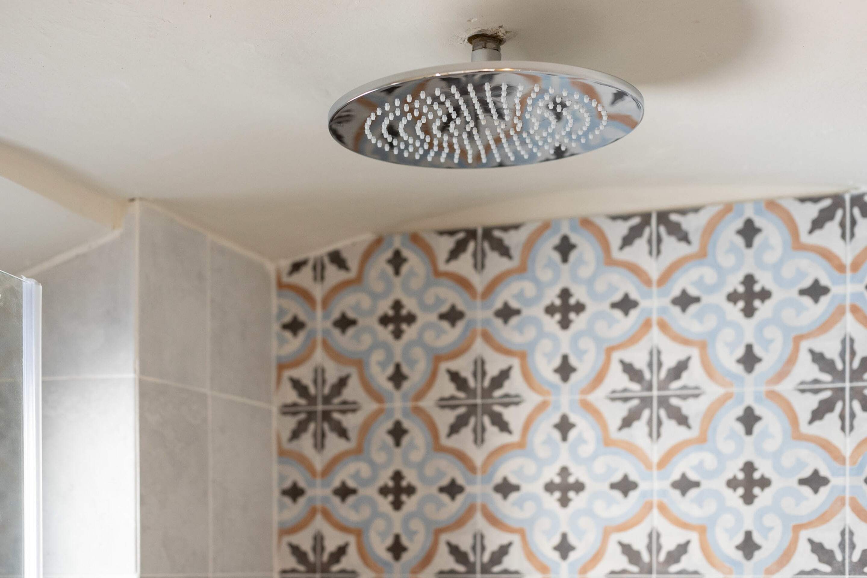 A bathroom with patterned tiles and a showerhead.