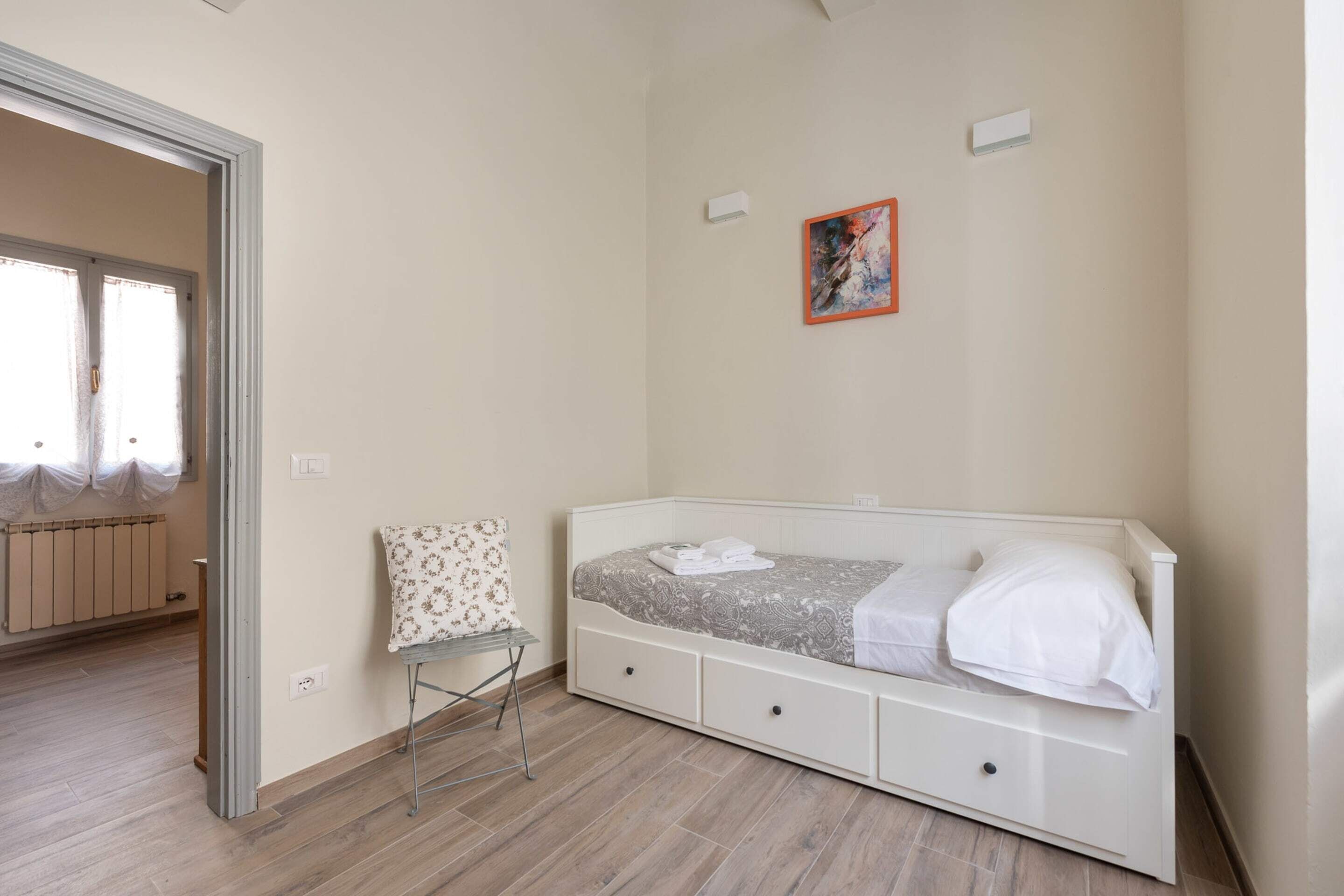 A bedroom with a bed, a chair, a radiator, and a painting on the wall.