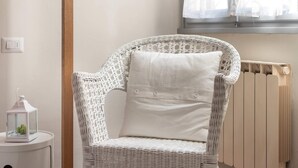 A wicker chair with a cushion, a white side table with a lantern, and a radiator. - Sanzanobi Apartment (Florence)