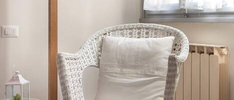 A wicker chair with a cushion, a white side table with a lantern, and a radiator.