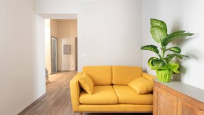 A modern living room with a mustard yellow sofa, a wooden cabinet, and a large green plant. - Sanzanobi Apartment (Florence)