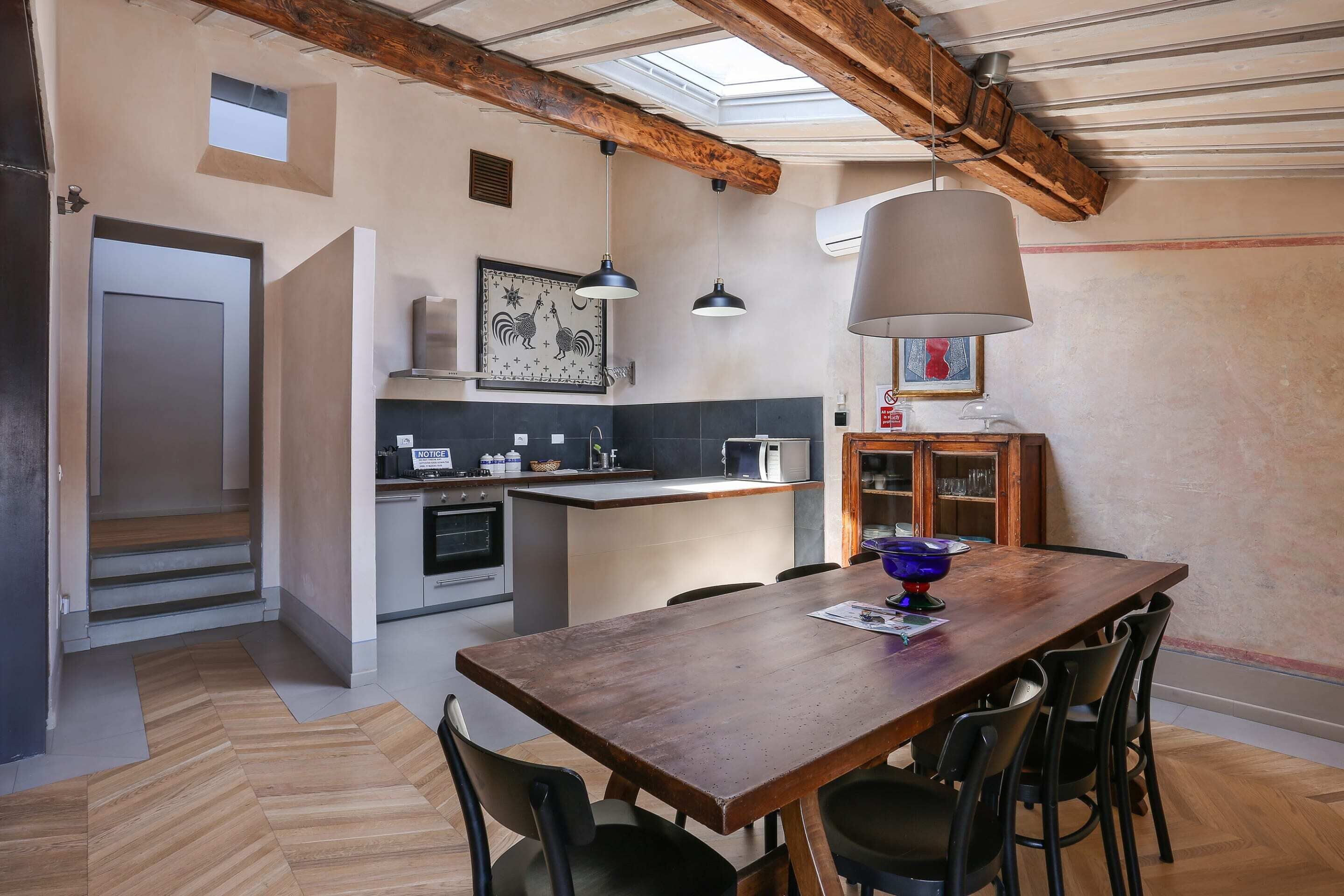 Une cuisine avec une table et des chaises en bois, un petit îlot central et des luminaires suspendus.