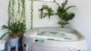 Ein Spa-Zimmer mit Whirlpool, Blumentöpfen und einem Fenster mit Blick auf Grünflächen.