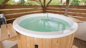 Ein hölzernes Whirlpool mit einer Uhr an der Wand, umgeben von einer Holzterrasse und einem Holzzaun.