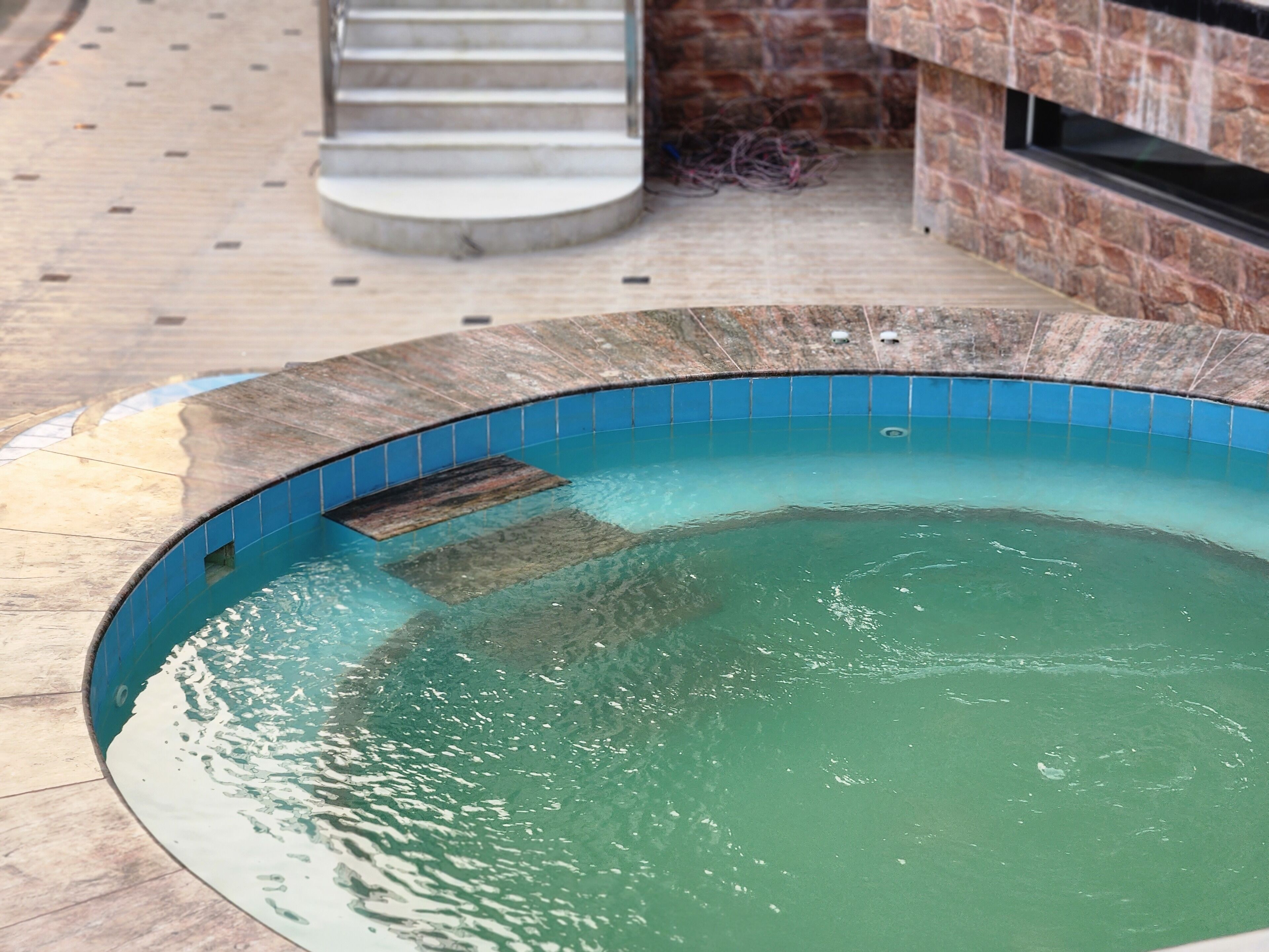 A swimming pool with a tiled edge, a stone wall, and a staircase in the background.