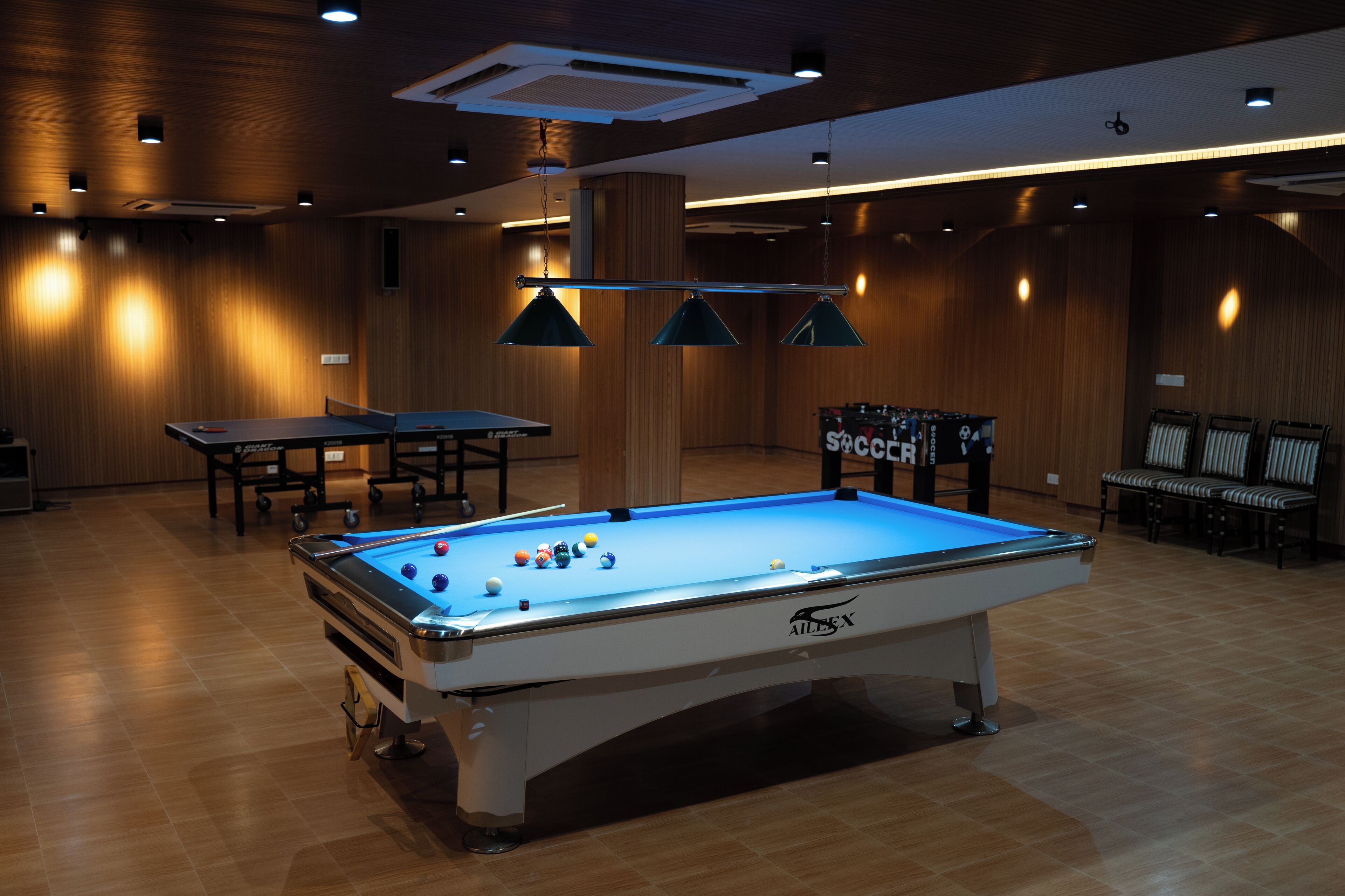 A pool table with balls, a table tennis table, and seating in a room with wooden walls and ceiling lights.