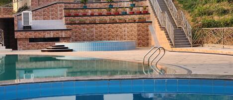 A swimming pool with a stone wall and a staircase leading to a building.