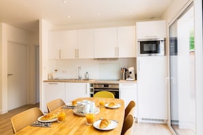 A modern kitchen with white cabinets, a wooden dining table, and breakfast items.