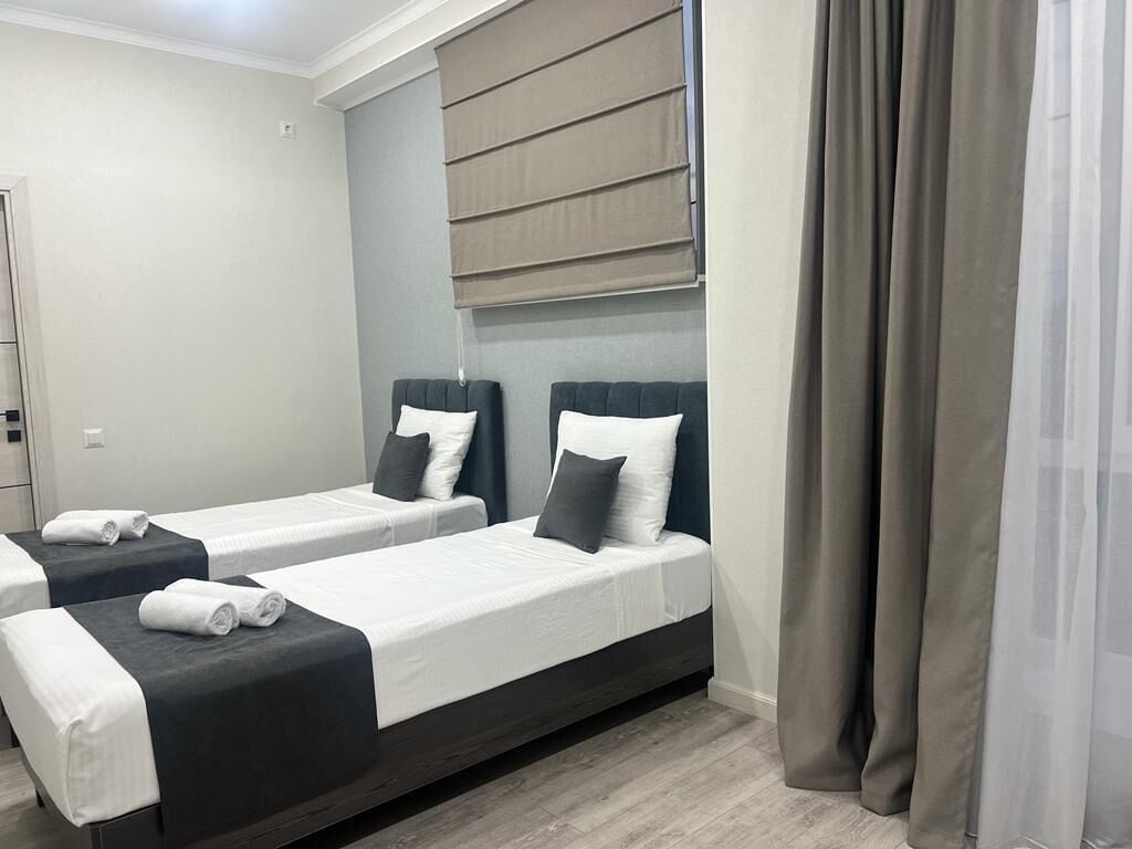 Quarto de hotel com duas camas de solteiro, cada uma com cabeceira escura, roupa de cama branca e uma toalha enrolada sobre a cama.