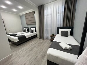 A hotel room with two beds, a small table, and a window with curtains. - Urban Hotel (Bishkek)
