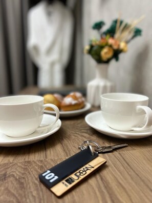 A table with two white cups and saucers, a small plate with pastries, and a keychain with "101 URBAN" on it. - Urban Hotel (Bishkek)