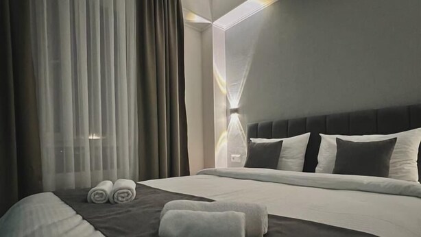 A modern hotel room with a large bed, a headboard with multiple pillows, and a large window with sheer curtains. - Urban Hotel (Bishkek)