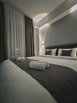 Ein modernes Hotelzimmer mit einem großen Bett, einer Kopfteil mit vielen Kissen und einem großen Fenster mit durchsichtigen Vorhängen.