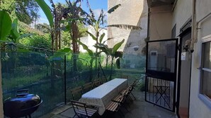 A balcony with a table and chairs, surrounded by greenery and a view of a building.