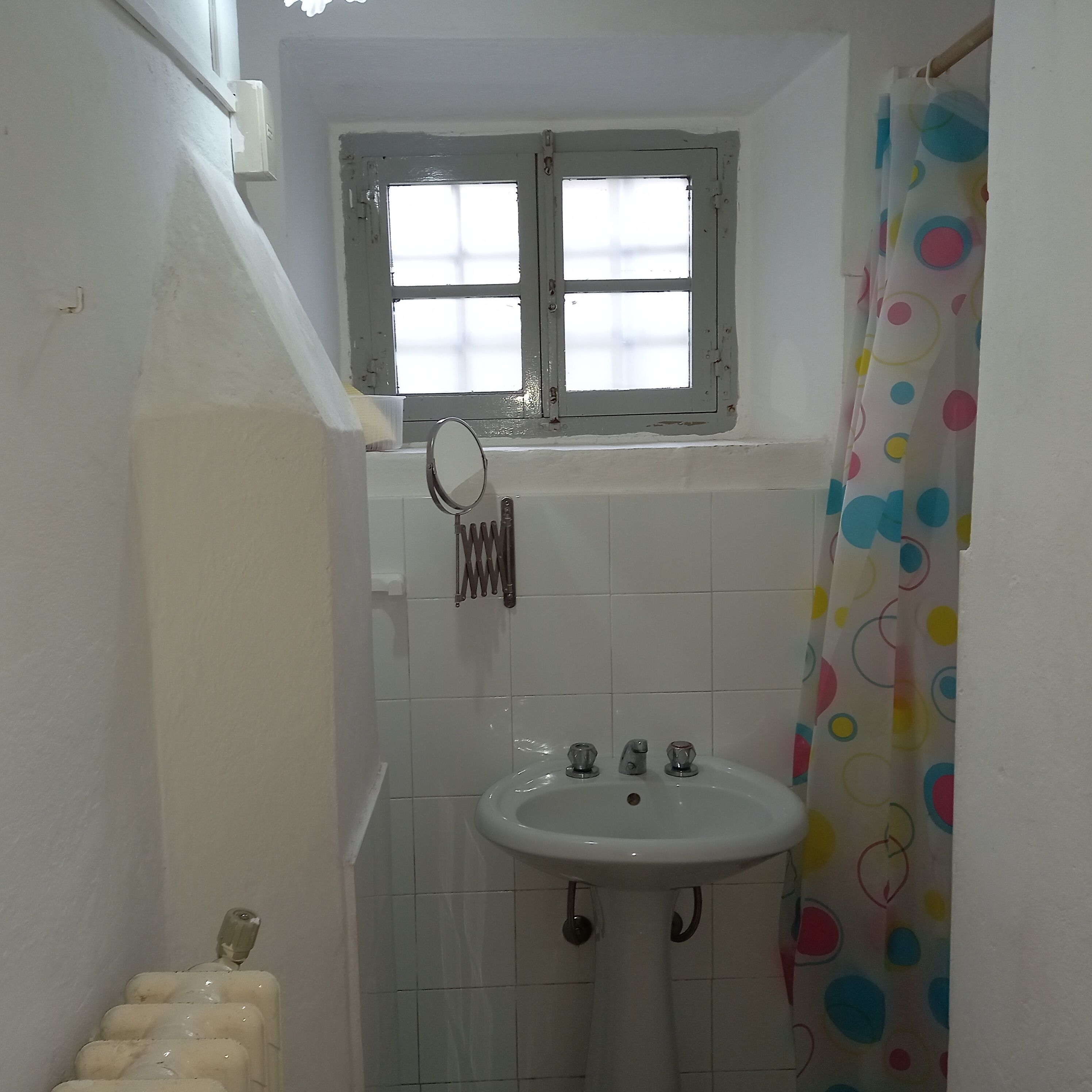 A small bathroom with a white sink, a window above the mirror, and a shower curtain with a polka dot pattern.