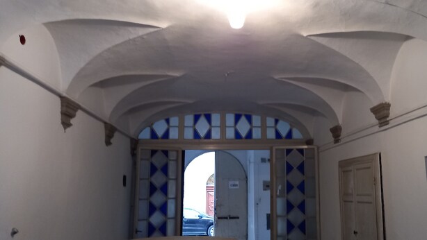 An arched hallway with a patterned door and a view of a street outside.