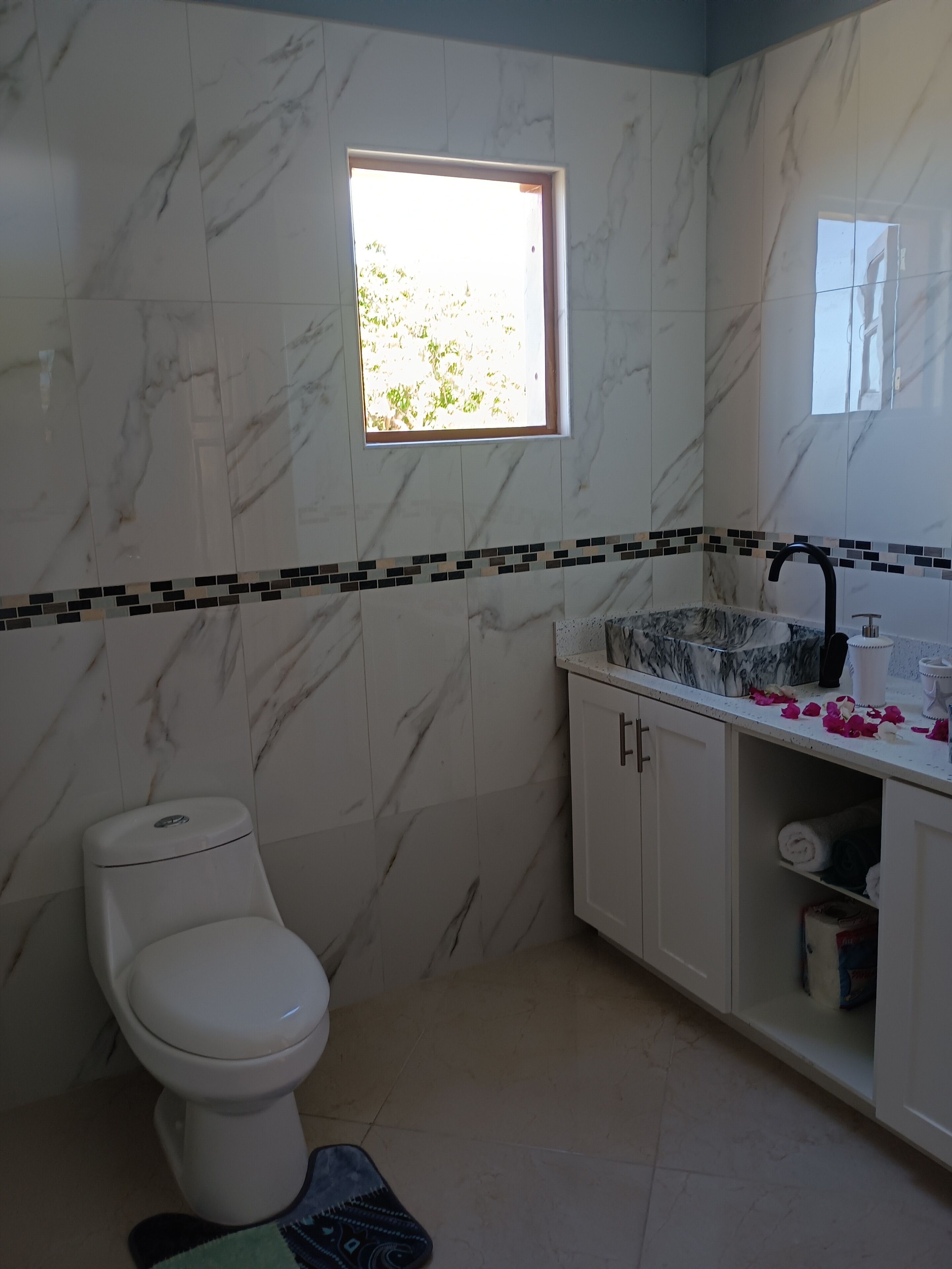 Ein Badezimmer mit Toilette, einem Waschbecken mit schwarzem Wasserhahn und einem kleinen Fenster.