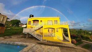 Ein gelbes, zweistöckiges Haus mit Balkon, Treppe und Swimmingpool.