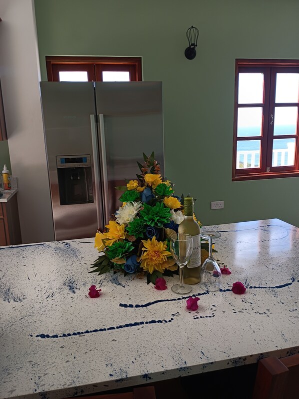 A kitchen with a stainless steel refrigerator, a bouquet of artificial flowers, a wine bottle, and a glass on the countertop.