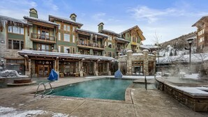 Un área de piscina con una fuente de piedra, rodeada de edificios de varios pisos con balcones y zonas de estar cubiertas.