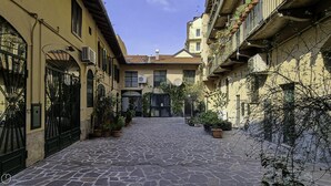 Uma rua de paralelepípedos estreita, ladeada por edifícios com varandas e plantas em vasos.