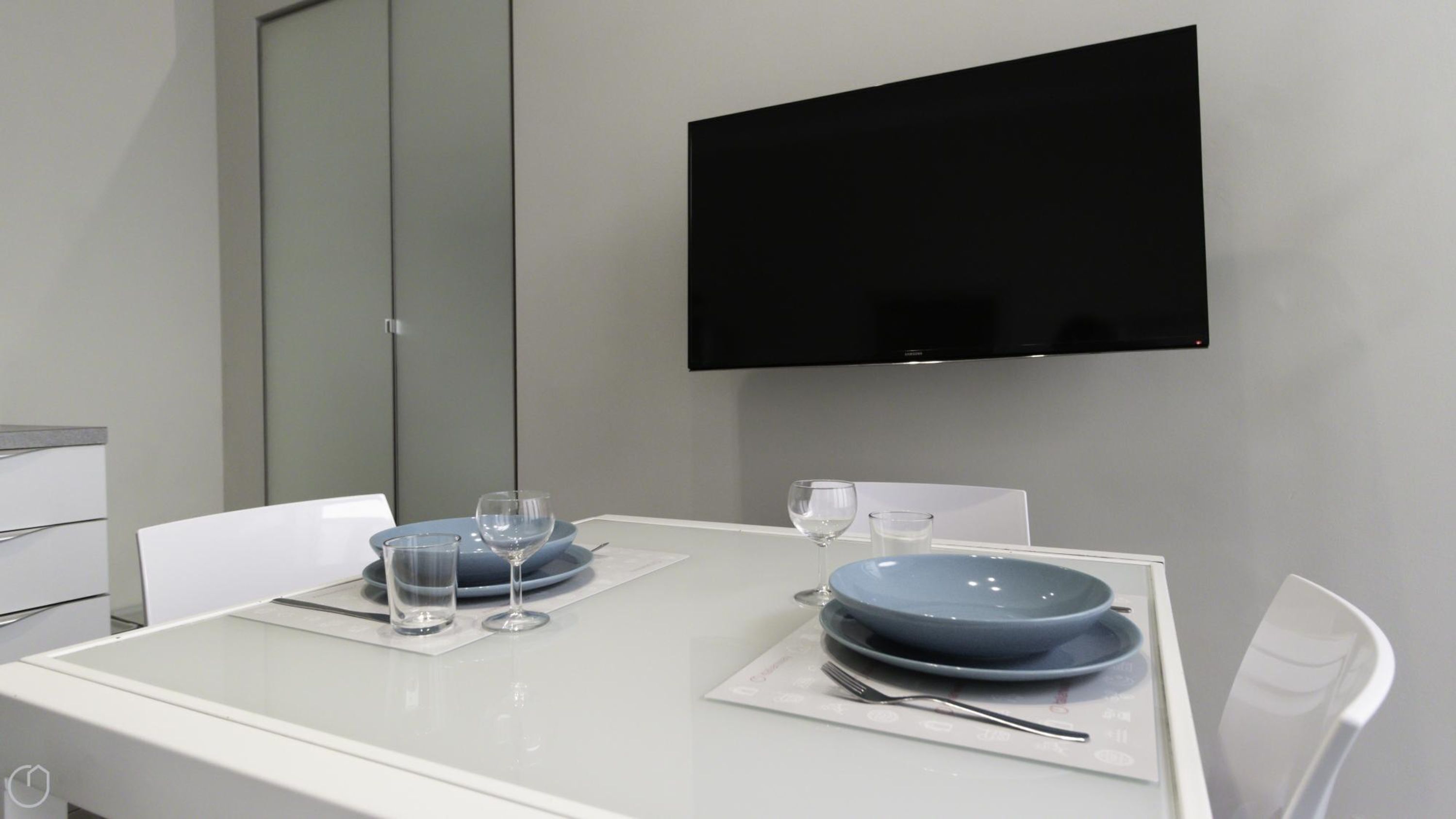 A modern dining area with a white table set for two, featuring blue plates and clear glasses.