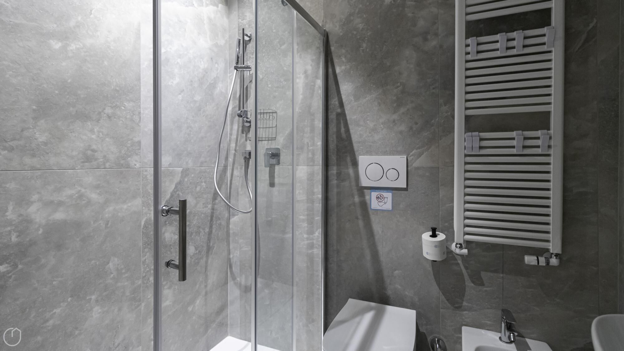 Un baño moderno con cabina de ducha de vidrio, toallero, dispensador de papel higiénico y lavamanos.
