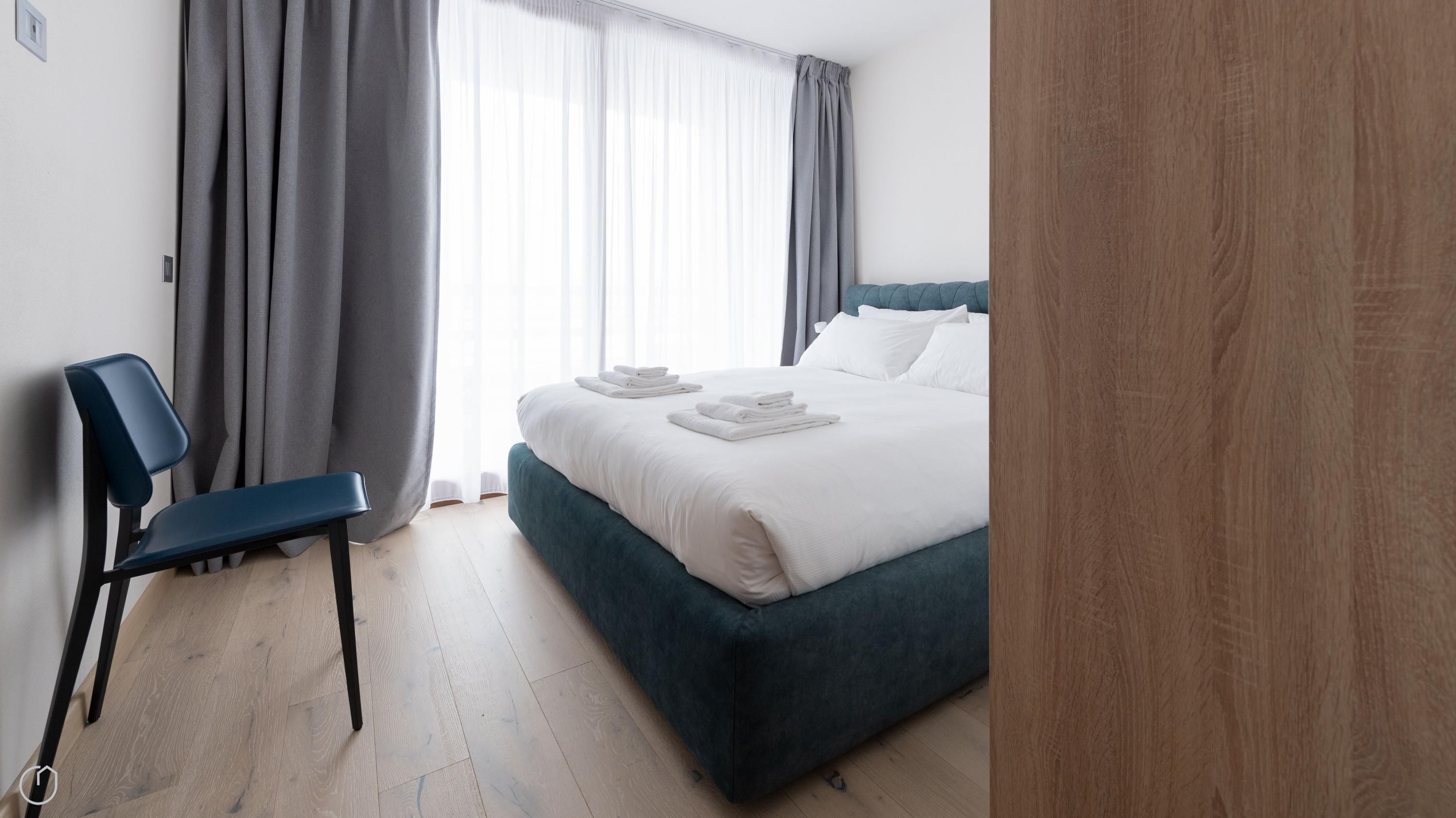 A hotel room with a bed, a chair, and a wooden door.
