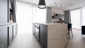 Une cuisine moderne avec un îlot en marbre, des meubles de couleur grise et un luminaire suspendu.
