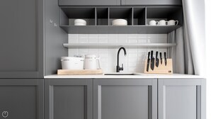 Une cuisine avec des meubles gris, un plan de travail blanc, un évier, une machine à café, une bouilloire et un bloc à couteaux.