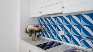 A kitchen with white cabinets, a blue and white patterned backsplash, and a vase with flowers on the countertop. - Villa Blue Sea Amalfi (Ravello)