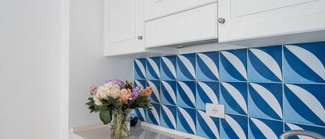 A kitchen with white cabinets, a blue and white patterned backsplash, and a vase with flowers on the countertop.