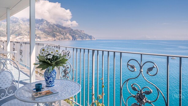 A balcony with a view of the sea, a table with a vase of flowers, and a chair. - Villa Blue Sea Amalfi (Ravello)