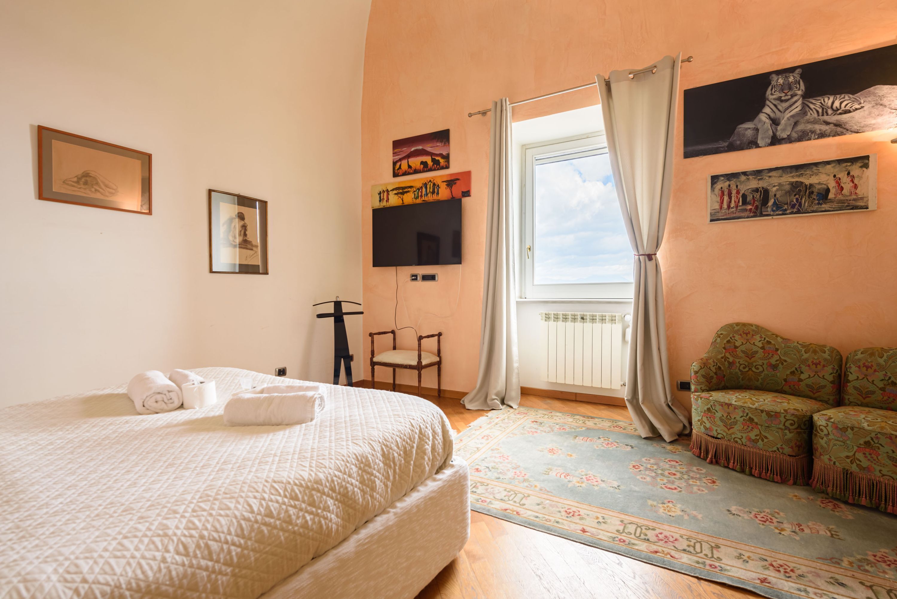 A bedroom with a bed, a chair, a sofa, and a window with curtains.