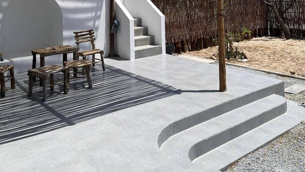 A modern outdoor seating area with a pergola, a staircase leading to a covered area, and a view of the surrounding landscape. - My Hoa Oceanfront Home (Vinh Hai)