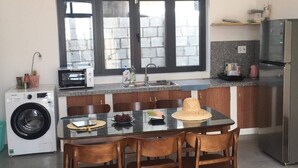 A compact kitchen with a dining table, chairs, a washing machine, a microwave, and a refrigerator. - My Hoa Oceanfront Home (Vinh Hai)