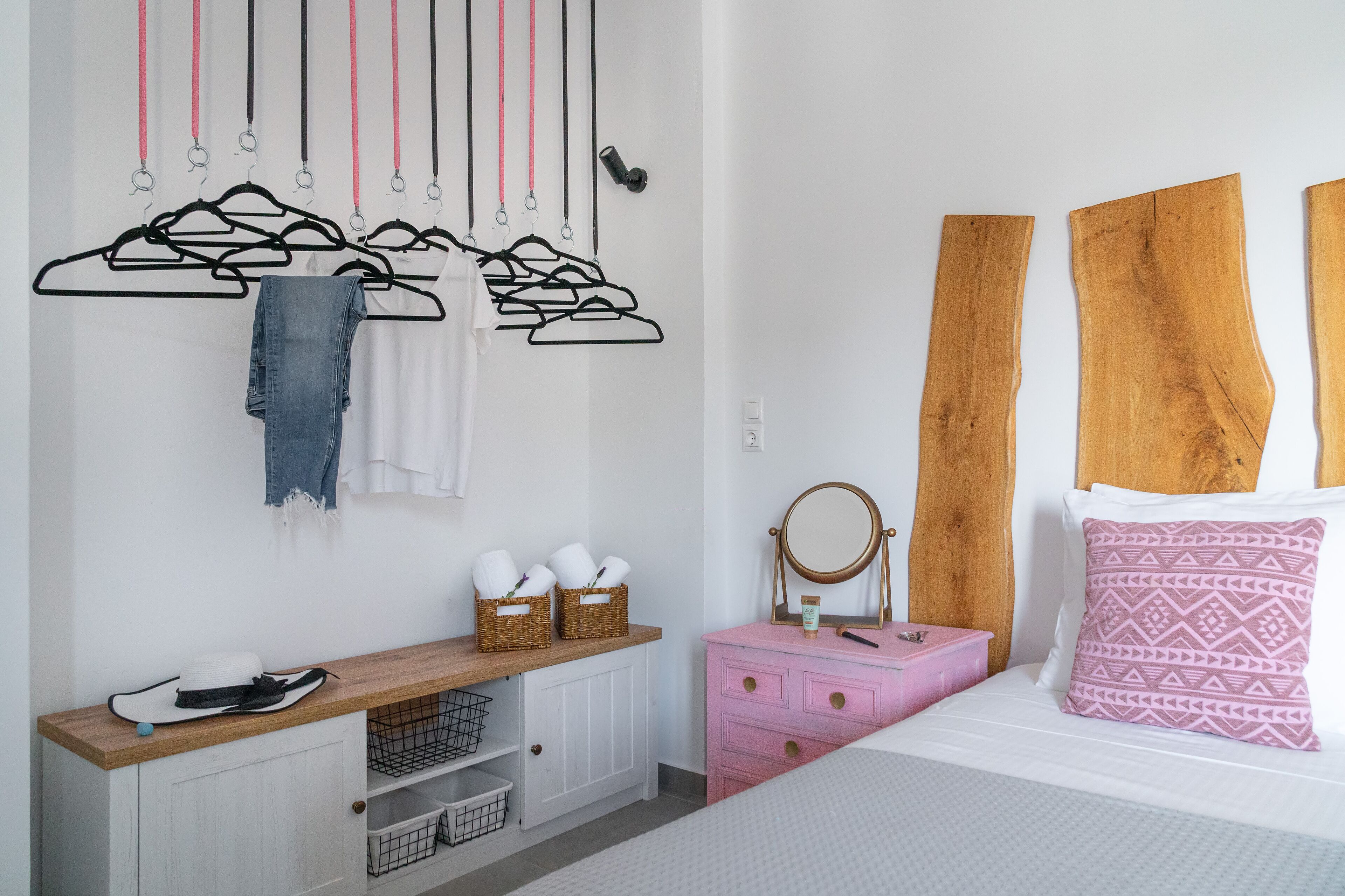 A bedroom with a wooden headboard, a pink dresser, a mirror, and a bed with a patterned pillow.