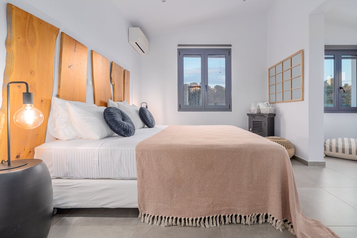 Une chambre à coucher avec un lit, une table de chevet, une lampe et une fenêtre donnant sur un beau paysage.